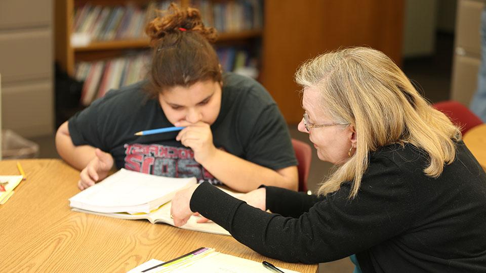 一名女性JCAE志愿者与一名女学生一起复习教科书中的材料