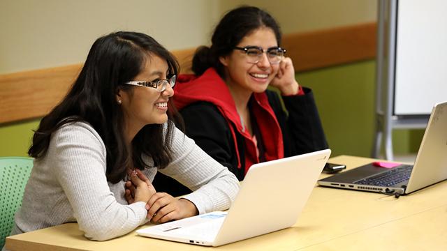 教室里，两个微笑着拿着笔记本电脑的女学生