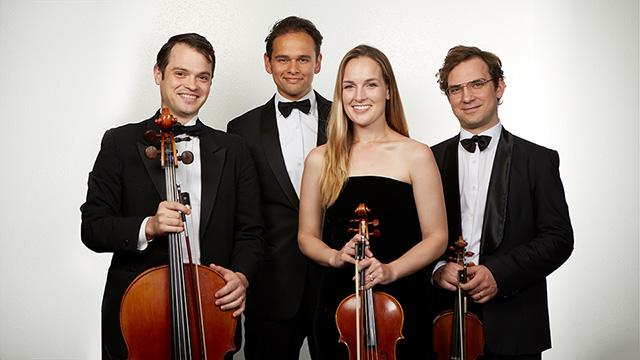 the 4 members of Opus 76 wearing black tie stand smiling at the camera while holding their instruments